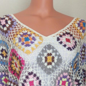 May include: A white crochet poncho with colourful granny squares. The poncho has a v-neck and fringe trim.