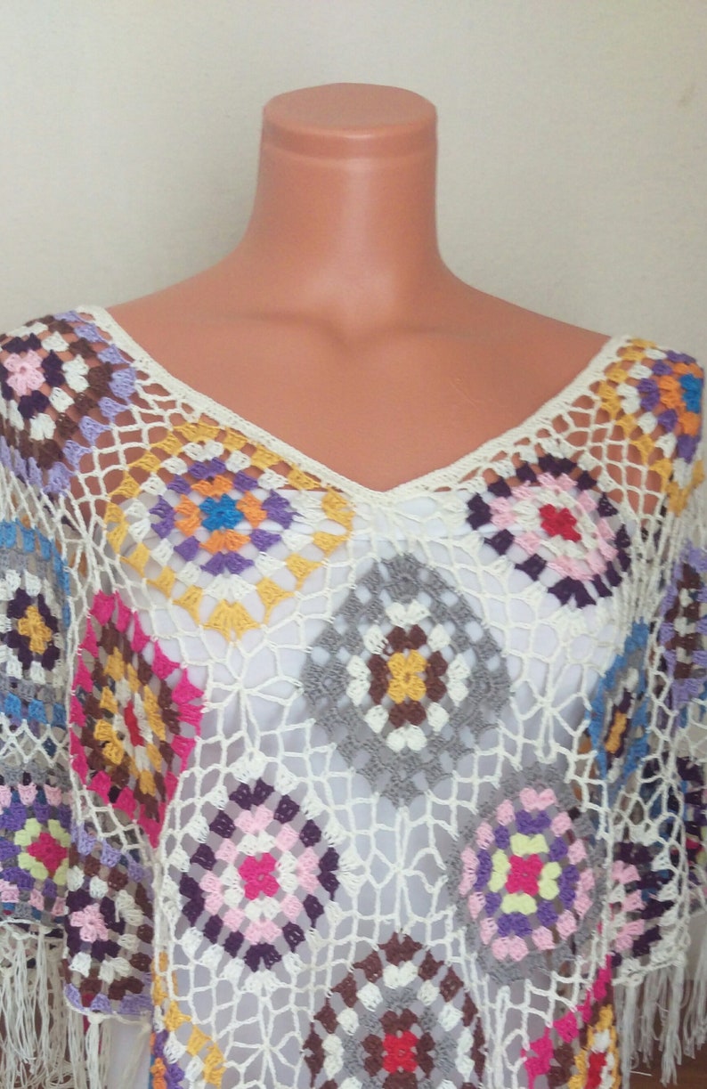 May include: A white crochet poncho with colourful granny squares. The poncho has a v-neck and fringe trim.