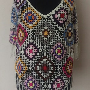 May include: A white crochet top with a colourful geometric pattern. The top has a V-neck and fringe trim.