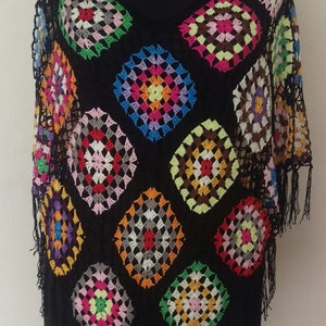 May include: A black crochet top with colourful granny squares. The top has a V-neck and short sleeves. The bottom of the top has fringe.