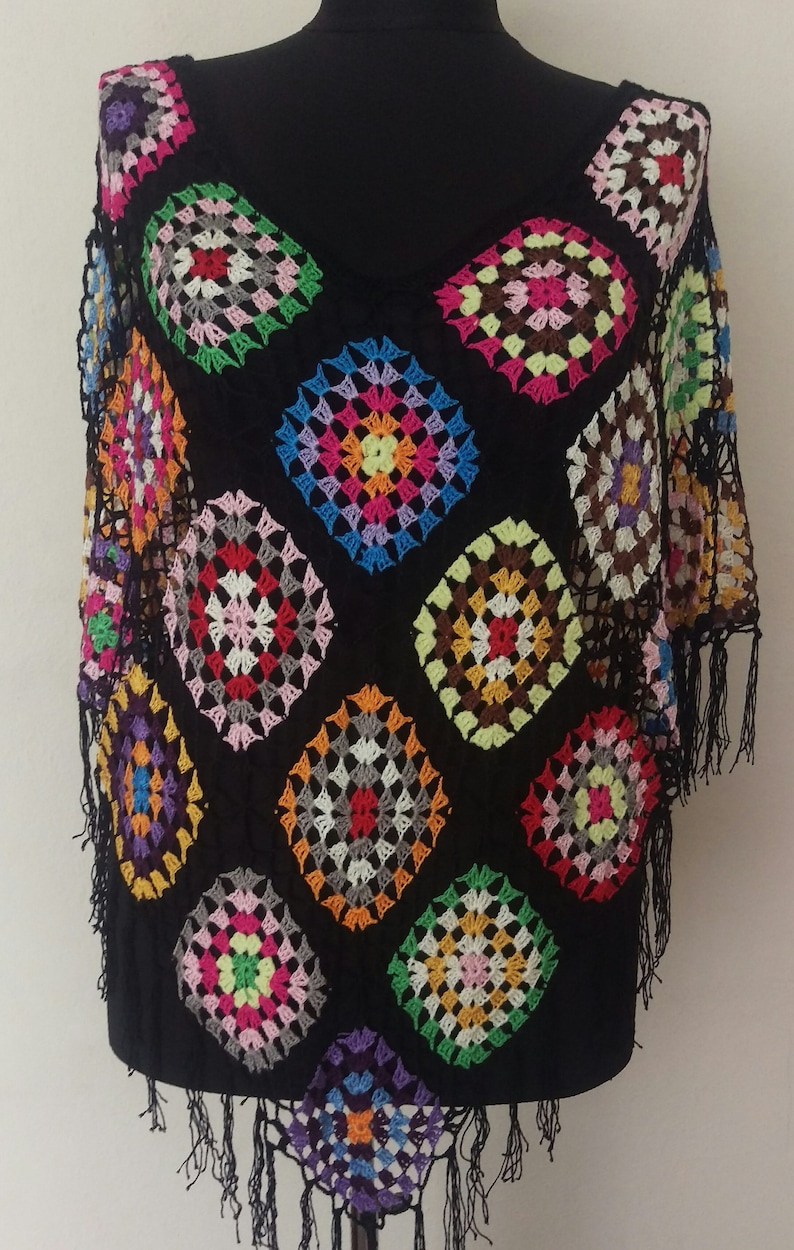 May include: A black crochet top with colourful granny squares. The top has a V-neck and short sleeves. The bottom of the top has fringe.