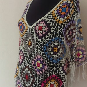May include: A white crochet poncho with colourful geometric patterns and fringe trim.