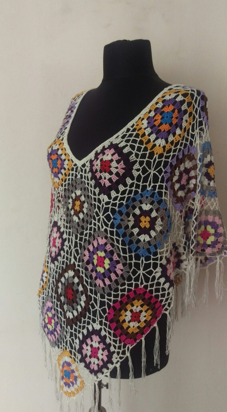 May include: A white crochet poncho with colourful geometric patterns and fringe trim.