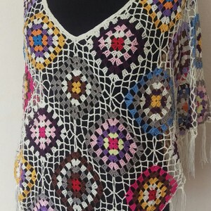 May include: A white crochet poncho with colourful granny squares. The poncho has a v-neck and fringe trim.