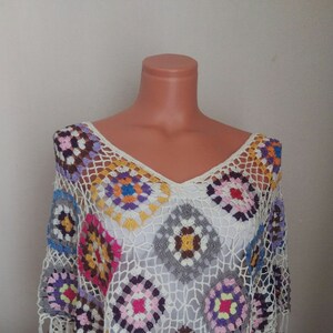 May include: A white crochet top with a colourful geometric pattern. The top is made of a lightweight, airy fabric and has a loose, flowing fit.