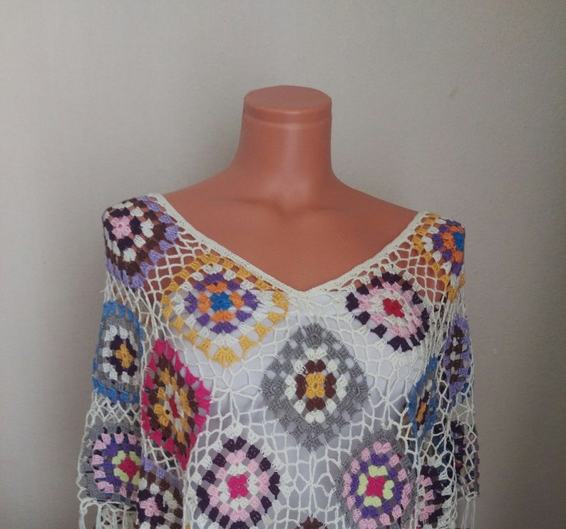 May include: A white crochet top with a colourful geometric pattern. The top is made of a lightweight, airy fabric and has a loose, flowing fit.