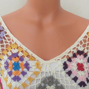 May include: A crocheted top with a V-neck and a colourful geometric pattern. The top is made of white yarn with multi-coloured squares.