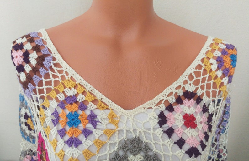 May include: A crocheted top with a V-neck and a colourful geometric pattern. The top is made of white yarn with multi-coloured squares.
