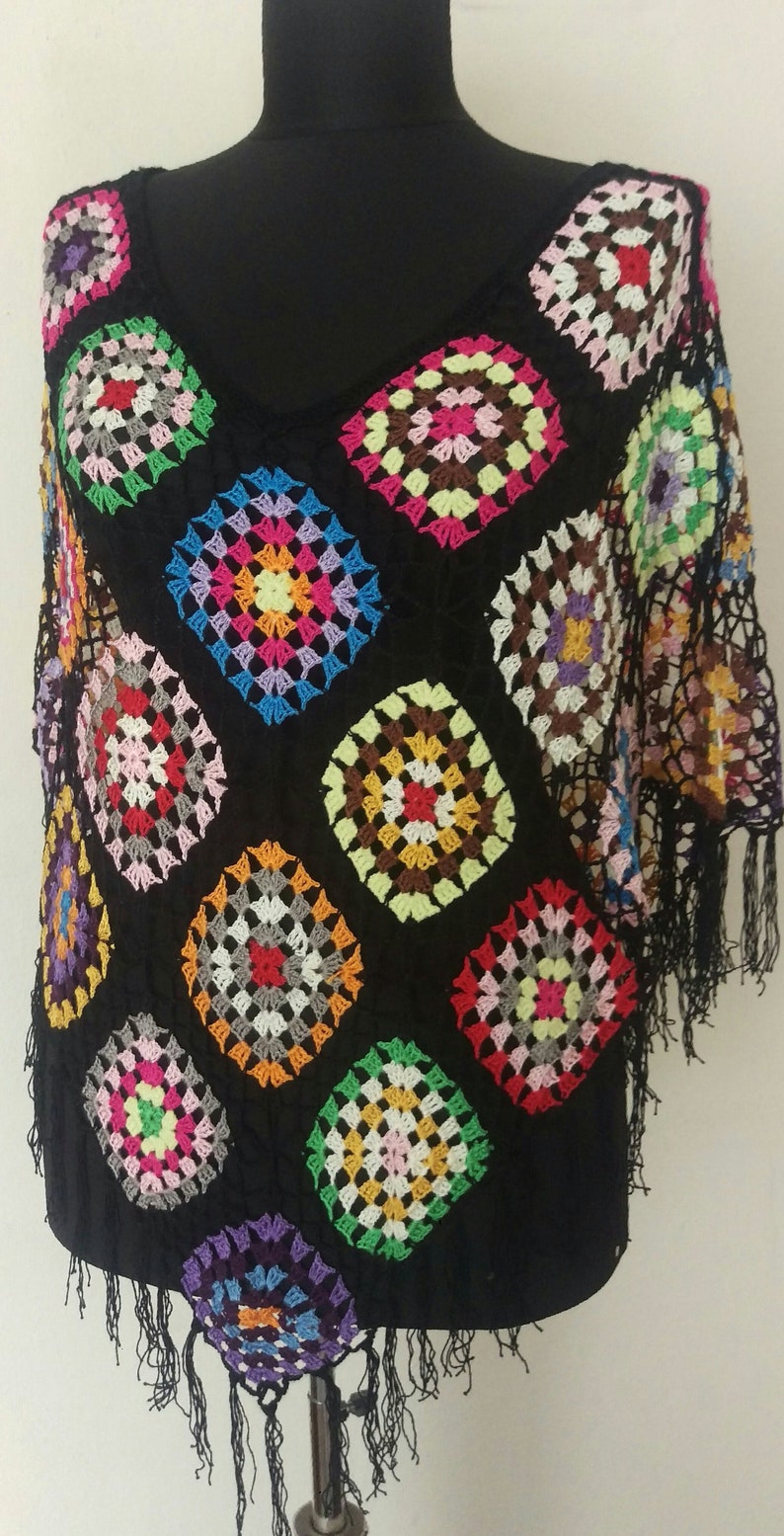 May include: A black crochet poncho featuring colourful granny squares. The poncho has a fringe trim and is made with a variety of colours, including red, blue, green, yellow, and pink.