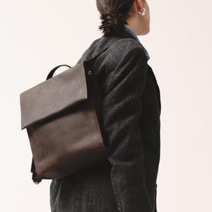 Woman in dark blazer and jeans wearing a brown chocolate leather backpack with flap closure by Taksuba.
