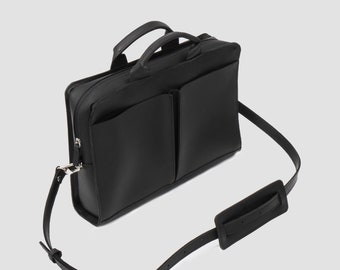 May include: Black briefcase with two front pockets, a top handle, and a detachable shoulder strap. The bag has a silver zipper and buckle. The shoulder strap has a padded shoulder rest for comfort.