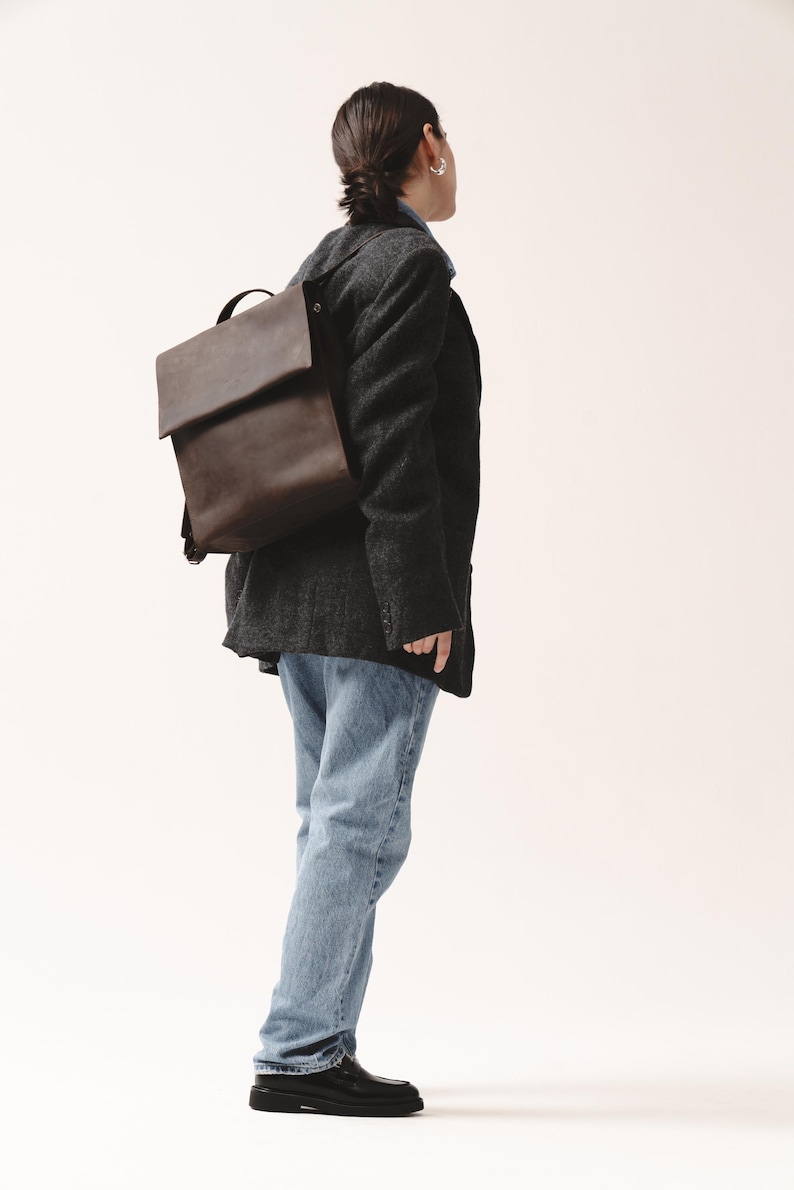 Woman in dark blazer and jeans wearing a brown chocolate leather backpack with flap closure by Taksuba.