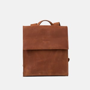 front view of Fi leather backpack in cognac brown with structured square flap design and top handle, crafted from smooth, durable full-grain leather