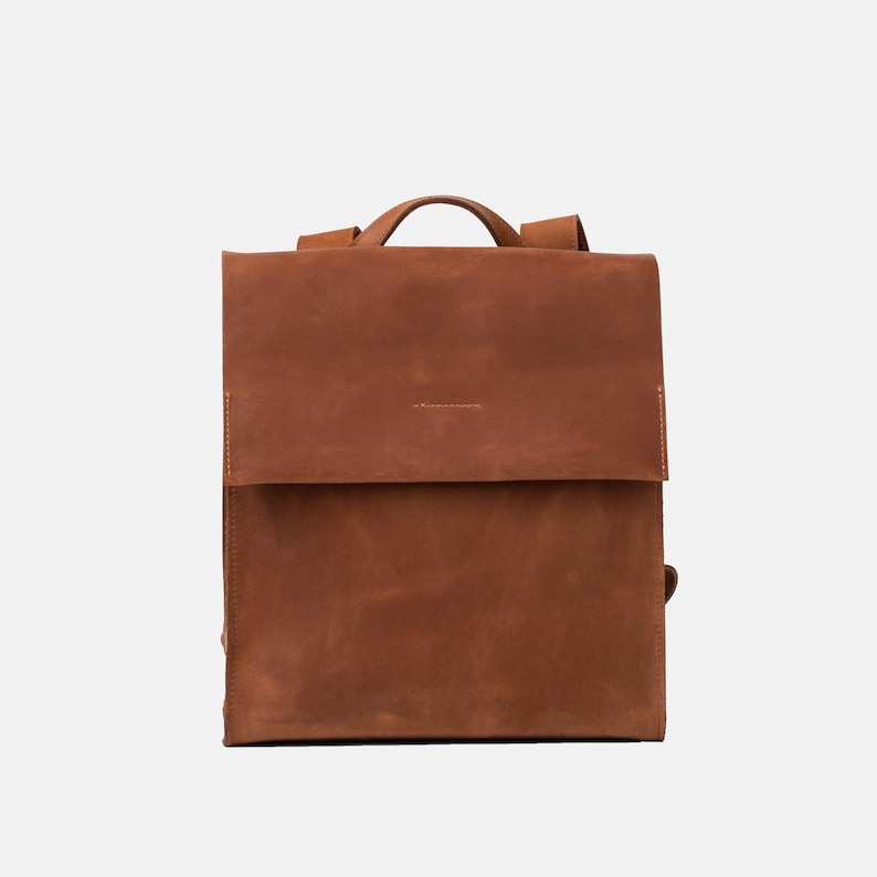 front view of Fi leather backpack in cognac brown with structured square flap design and top handle, crafted from smooth, durable full-grain leather