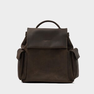 front view of European leather backpack in dark brown with flap closure, rounded top handle, and dual side pockets, handcrafted from soft full-grain leather