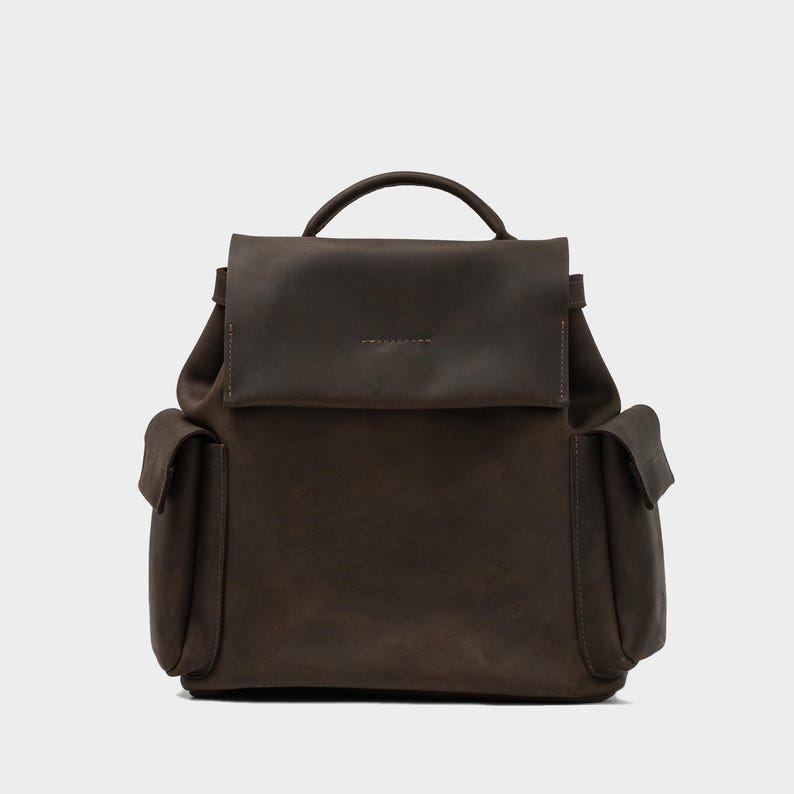 front view of European leather backpack in dark brown with flap closure, rounded top handle, and dual side pockets, handcrafted from soft full-grain leather