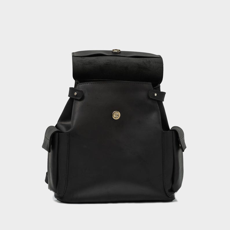 front view of black European leather backpack with flap open, showcasing magnetic snap closure and top-loading main compartment with dual side pockets