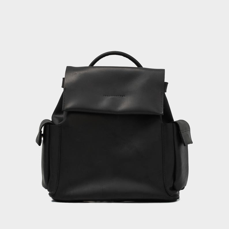 front view of European leather backpack in black with flap closure, top handle, and two side pockets, crafted from premium grain-textured leather