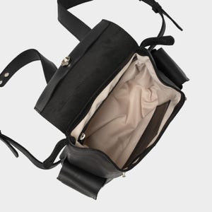 interior view of black European leather backpack with flap open, showing beige waterproof lining, internal zip pocket, and slip pocket for organization