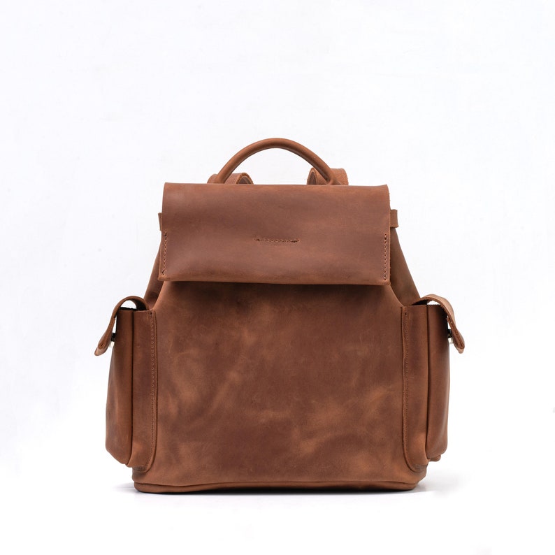 Elegant brown leather backpack with a smooth finish and sturdy handle, showcasing a minimalist front flap design suitable for professional and casual wear.