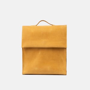 front view of Fi leather backpack in mustard yellow with clean flap design, top handle, and structured silhouette, handcrafted from smooth full-grain leather