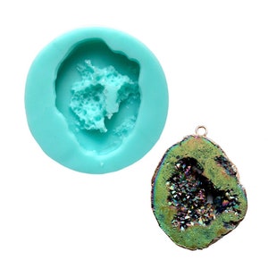 May include: A silicone mold for making resin jewelry in the shape of a geode with a crystal-like interior. The mold is light blue and the geode is green with iridescent crystals.