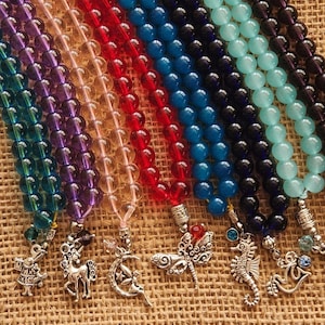 May include: Seven strands of colorful beaded necklaces with silver charms. The charms include a unicorn, a dragonfly, a crescent moon, a seahorse, an anchor, a bird, and a dragon.