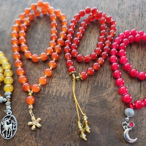 May include: Four beaded necklaces in shades of yellow, orange, and red. Each necklace features round beads and a decorative pendant. The necklaces are displayed on a wooden surface, showcasing their colors and textures.