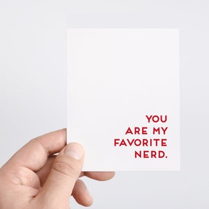Pu&ograve; includere: Un biglietto bianco con il testo "You are my favorite nerd." in rosso.