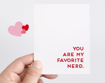 May include: A white card with red text that reads "You are my favorite nerd."  Two pink hearts and one red heart are in the top left corner of the card.