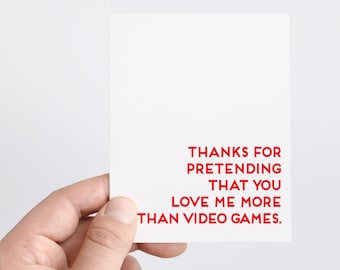 May include: White card with red text that reads "Thanks for pretending that you love me more than video games."