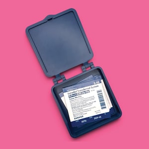 May include: A dark blue plastic hinged case containing multiple square white and blue medical patches. The label reads Estradiol Transdermal System, Delivers 0.05 mg/day, Twice Weekly, Sandoz, with a barcode and expiration date of 2029-03.