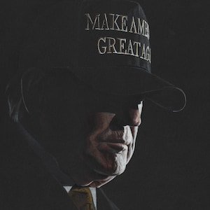 May include: A dark-toned portrait of a person wearing a black baseball cap with the text "MAKE AMERICA GREAT AGAIN" embroidered in white. The subject is dressed in a dark suit jacket with a visible yellow necktie, captured in low-key lighting.