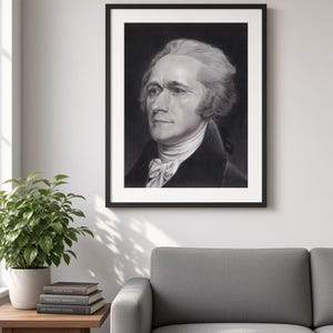May include: A framed black and white charcoal-style portrait print of Alexander Hamilton, featuring a man with wavy hair, a high-collared coat, and a cravat, presented in a simple black frame with a white mat board border.