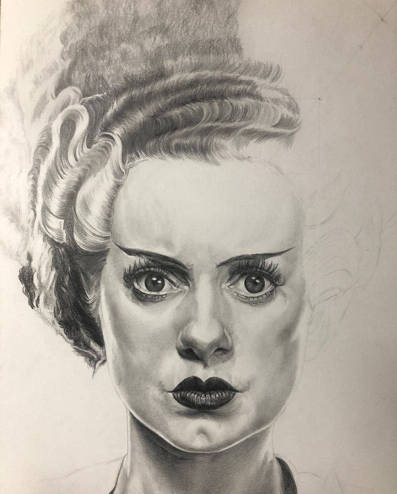 Peut inclure: Un dessin au crayon graphite repr&eacute;sentant une personne avec une coiffure haute et volumineuse dot&eacute;e d'une m&egrave;che blanche. Le portrait pr&eacute;sente des ombres d&eacute;taill&eacute;es sur le visage, des l&egrave;vres sombres et des cils d&eacute;finis, le c&ocirc;t&eacute; droit &eacute;tant esquiss&eacute;.