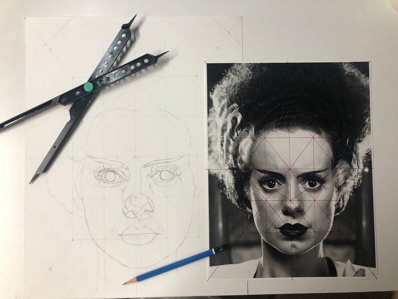 Peut inclure: Un portrait en noir et blanc de la fianc&eacute;e de Frankenstein avec des lignes de grille g&eacute;om&eacute;triques superpos&eacute;es, accompagn&eacute; d'un croquis au crayon du m&ecirc;me visage &agrave; gauche, d'un compas noir et d'un crayon bleu sur la surface.