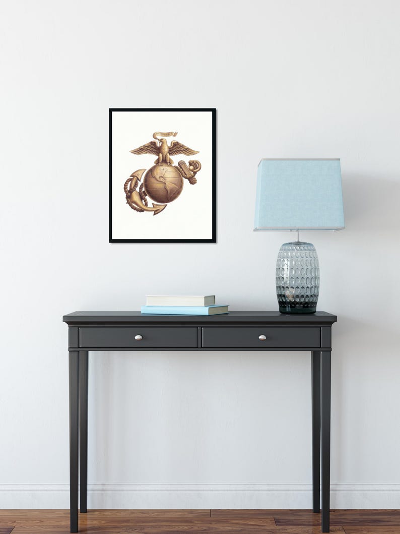 May include: A framed wall art print featuring the United States Marine Corps emblem in a bronze tone. The design displays a detailed eagle perched atop a globe, with a fouled anchor positioned behind the globe, all set against a white background.