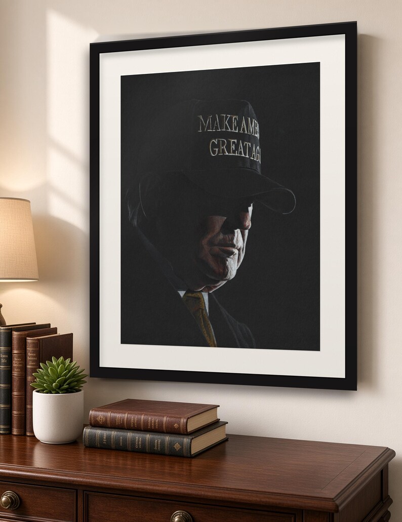 May include: A framed portrait print featuring a dark, moody side profile of a person wearing a dark baseball cap with the text MAKE AMERICA GREAT AGAIN embroidered in white. The subject wears a dark suit jacket and a gold-toned necktie.