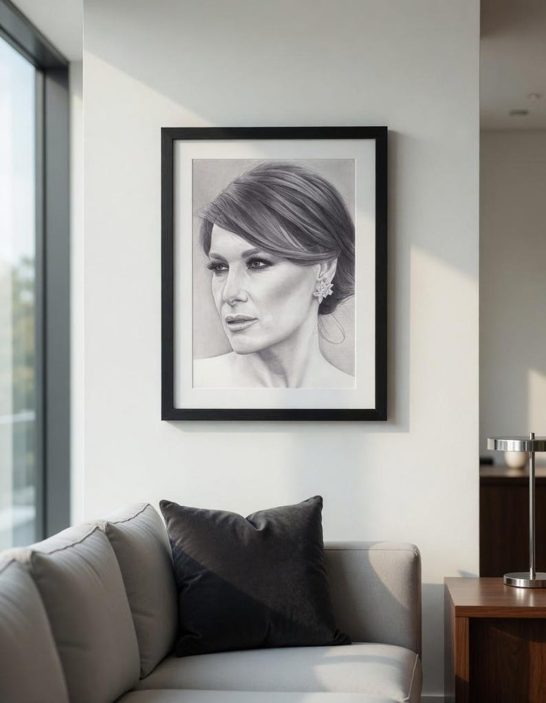 May include: A black and white charcoal portrait drawing of a person with styled hair and an earring, framed in a simple black frame. The artwork depicts a side profile view of the individual with detailed shading and realistic facial features.