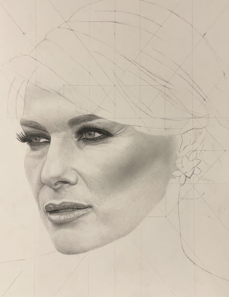 May include: A graphite pencil drawing of a face featuring detailed shading on the eyes, nose, and lips. The portrait includes visible geometric construction lines and grid marks across the forehead and hair area, with a floral earring.