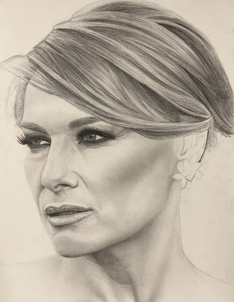 May include: A graphite pencil drawing of a person with short, layered hair, styled with a side part. The subject has defined eyebrows, long eyelashes, and a floral-shaped earring on the visible ear, rendered in shades of gray and white.