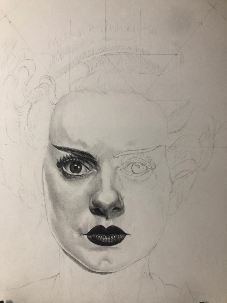 Peut inclure: Un dessin au crayon graphite d'un visage en cours de r&eacute;alisation. Le c&ocirc;t&eacute; droit pr&eacute;sente un &oelig;il tr&egrave;s d&eacute;taill&eacute; avec eye-liner, cils et peau ombr&eacute;e, tandis que le c&ocirc;t&eacute; gauche reste un contour l&eacute;ger. Les l&egrave;vres sombres sont ombr&eacute;es.