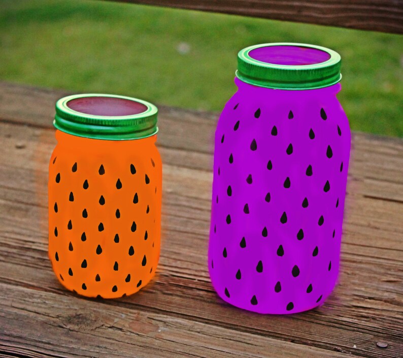 May include: Two glass jars painted to look like watermelons. The smaller jar is orange with black seeds and the larger jar is purple with black seeds.