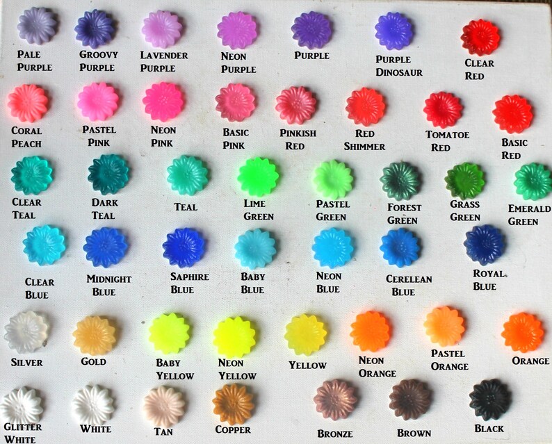 K&ouml;nnte beinhalten: Eine Karte mit 40 kleinen, blumenf&ouml;rmigen Kn&ouml;pfen in verschiedenen Farben, darunter Lila, Rosa, Rot, T&uuml;rkis, Gr&uuml;n, Blau, Gelb, Orange, Wei&szlig;, Schwarz, Silber, Gold, Kupfer und Bronze. Jeder Knopf ist mit seinem Farbnamen beschriftet.