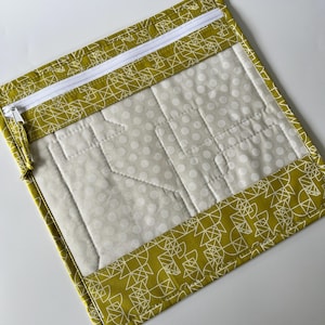 May include: A yellow zippered pouch with a white zipper and a clear vinyl window. The pouch is made of fabric with a geometric pattern in white on a yellow background. The window shows a white fabric with a white polka dot pattern.
