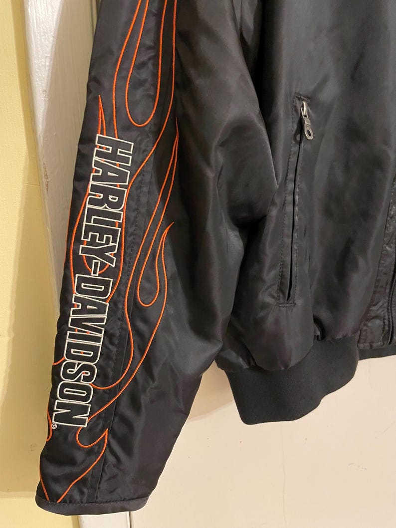 May include: Black bomber jacket with orange flame detailing and the Harley-Davidson logo on the sleeve.