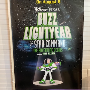 May include: A black and green movie poster for the Disney Pixar film "Buzz Lightyear of Star Command: The Adventure Begins". The poster features a cartoon image of Buzz Lightyear, a space ranger, standing in a spotlight against a starry background. The text "Never Fear, Buzz Is Here... On August 8" is at the top of the poster. The poster also includes the text "Starring Tim Allen".