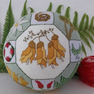 May include: A white sphere with a green background, featuring a variety of embroidered floral designs. The sphere is surrounded by green fern leaves and a red flower.