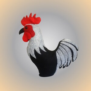 Puede incluir: Un juguete de gallo de fieltro con cresta y barbilla rojas, plumas negras y grises, y un fondo blanco.