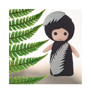 May include: A handcrafted felt doll featuring a black dress and a matching black headpiece, both adorned with a silver glitter fern leaf applique. The doll has a light beige face with two small black bead eyes and a simple stitched mouth.